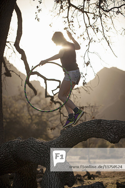 Junge Frau balanciert auf einem Ast mit einem Hoola-Hoop-Reifen  Malibu Creek State Park  Kalifornien  USA