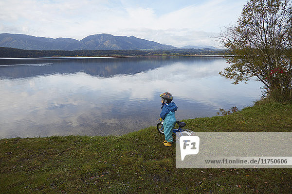 Young boy standing with bike beside lake