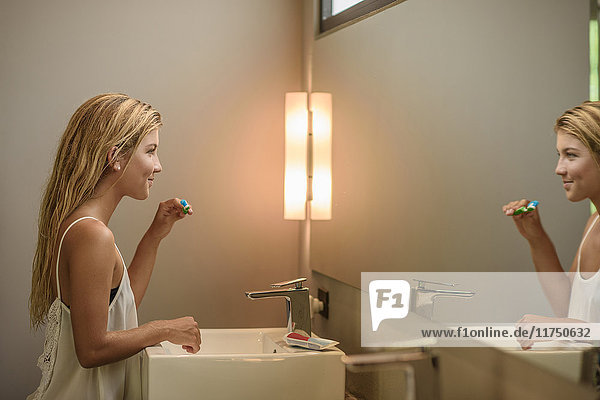 Junge Frau schaut beim Zähneputzen in den Badezimmerspiegel