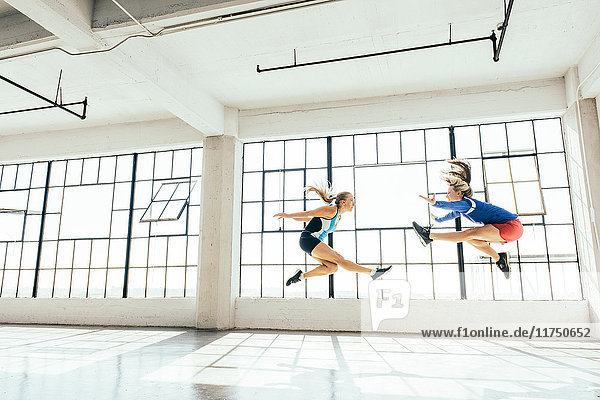 Niedrigwinkel-Seitenansicht von jungen Frauen im Fitnessstudio beim Ausfallschritt in der Luft