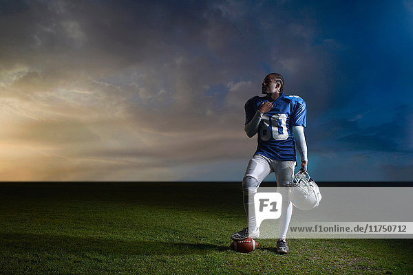 Porträt eines American-Football-Spielers  der mit dem Fuß auf dem Ball ruht