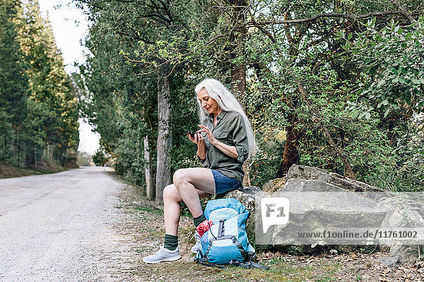 Ältere Backpackerin betrachtet Smartphone auf Waldstraße  Scandicci  Toskana  Italien