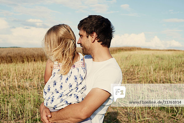Mature man carrying toddler daughter looking out from wheat field