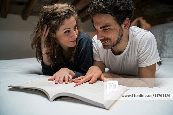 Junges Paar liegt im Bett und liest gemeinsam ein Buch