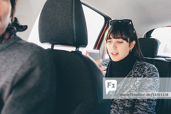 Frau auf dem Rücksitz im Auto mit Blick auf Smartphone