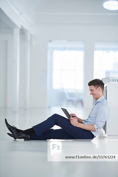 Mann im Büro sitzt auf dem Boden und benutzt ein digitales Tablett