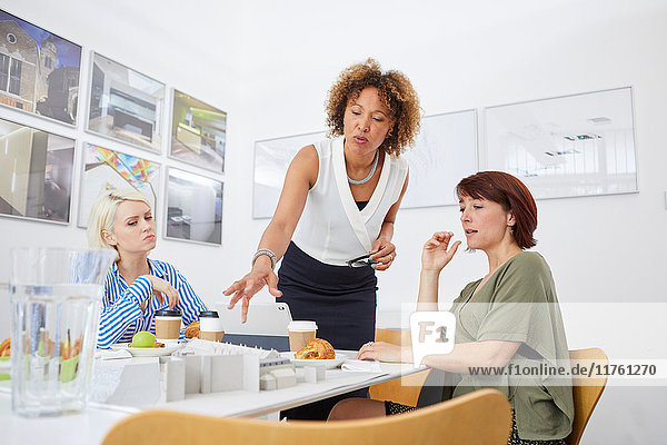 Ein weibliches Architektenteam zeigt bei einer Besprechung auf ein Architekturmodell auf dem Tisch