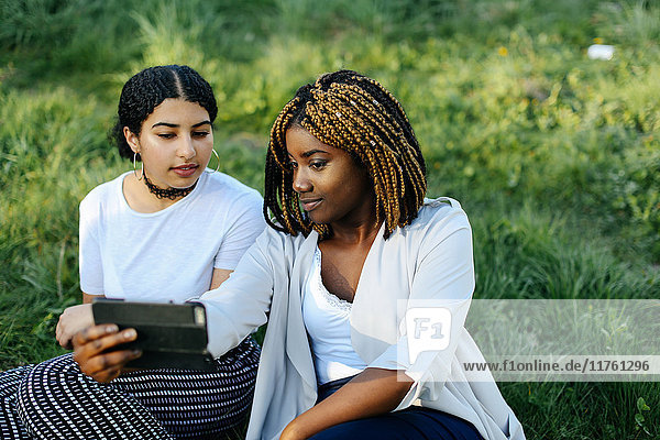 Zwei Teenager-Mädchen sitzen auf dem Rasen und schauen auf ein Smartphone