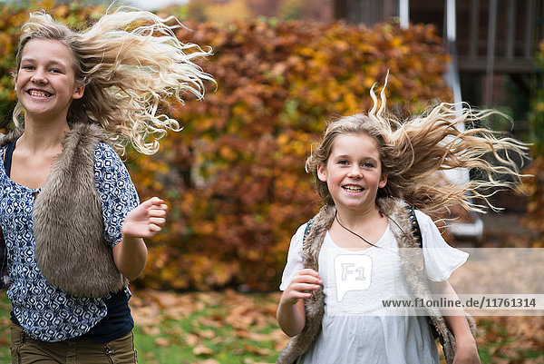 Zwei Schwestern mit langen blonden Haaren laufen im Herbstgarten