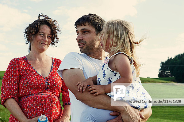 Pregnant couple in field with toddler daughter