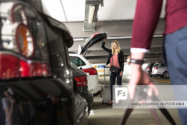 Young woman waiting for boyfriend at open car boot in airport carpark