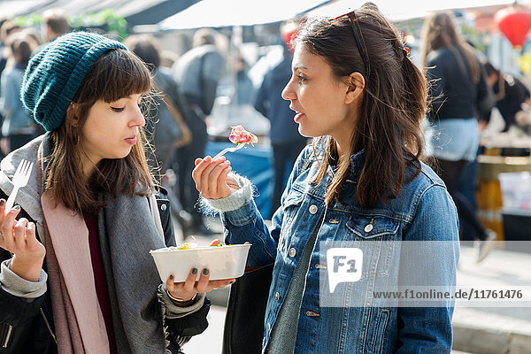 Zwei junge Frauen essen Essen zum Mitnehmen auf dem Markt