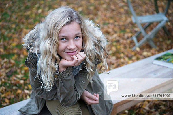 Porträt eines blonden Mädchens  das im Herbst auf einer Gartenbank sitzt