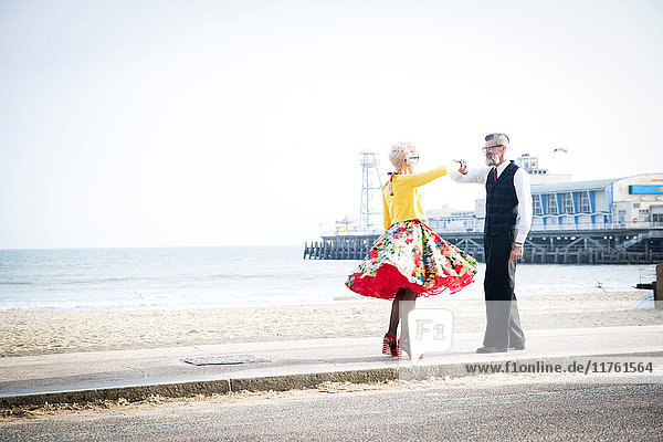 Paar im Vintage-Stil der 1950er Jahre  das sich an den Händen hält und am Strand tanzt