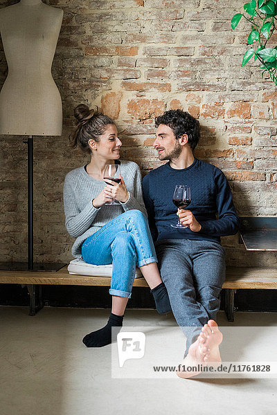 Junges Paar sitzt auf Bank mit Rotwein