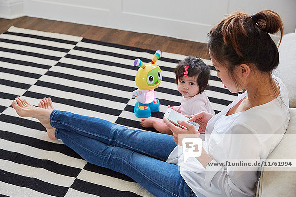 Frau mit kleiner Tochter sitzt auf dem Boden und nutzt den Touchscreen eines Smartphones