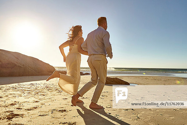 Ein erwachsenes Paar läuft am Strand entlang  Hand in Hand  Rückansicht  Kapstadt  Südafrika