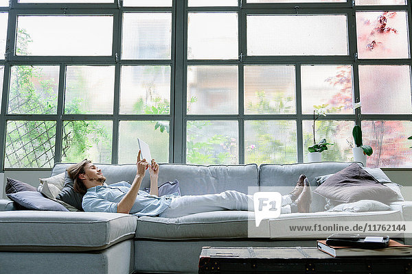 Auf Sofa liegender Mann mit digitalem Tablett