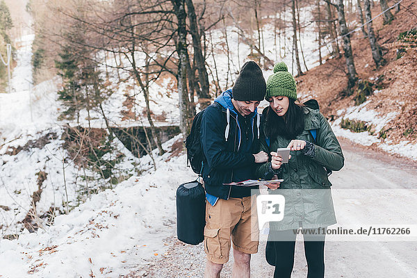 Hiking couple on snowy forest road looking at smartphone  Monte San Primo  Italy