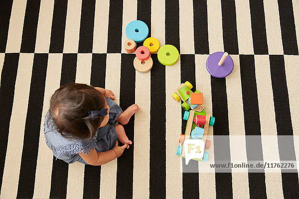 Draufsicht eines auf dem Teppich sitzenden Mädchens  das mit einer Spielzeugeisenbahn spielt