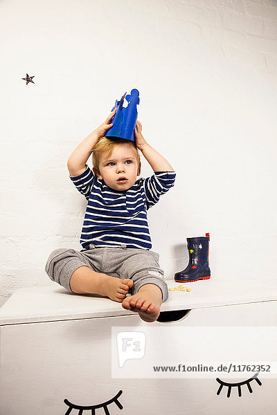 Male toddler sitting on toy chest putting on toy crown