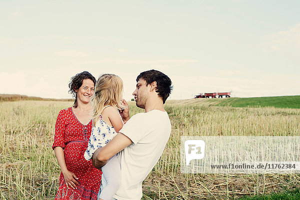 Pregnant couple in wheat field with toddler daughter