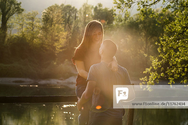 Paar am Fluss  junge Frau auf dem Zaun sitzend  dem jungen Mann zugewandt  lächelnd