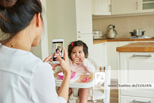 Over shoulder view of woman photographing baby daughter in high chair