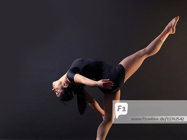 Low-Key-Schuss einer jungen Tänzerin  die sich im Stehen auf einem Bein nach hinten beugt