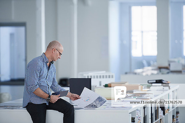 Man in open plan office looking at blueprint