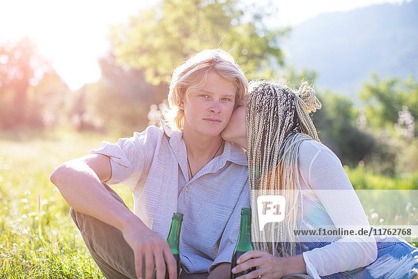 Romantic young couple sitting in field with bottled beer  Majorca  Spain