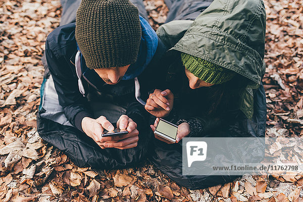 Wanderndes Paar in Schlafsäcken liegend und Smartphones betrachtend im Wald  Monte San Primo  Italien