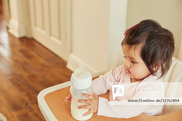 Mädchen hält Babymilchflasche auf Hochstuhl