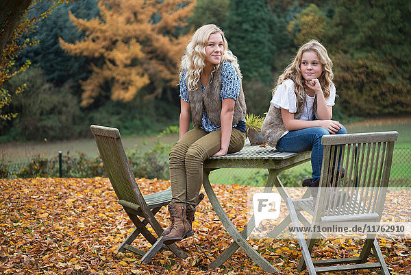 Porträt von zwei Schwestern  die auf einem Tisch im Herbstgarten sitzen