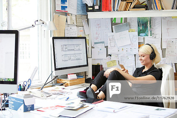 Designerin mit den Füßen auf dem Schreibtisch beim Blick auf das Smartphone