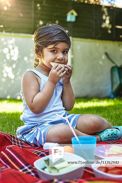 Porträt eines jungen Mädchens  das im Garten picknickt und ein Sandwich isst