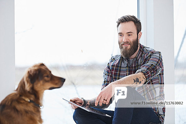 Junger männlicher Designer mit Hund im Designstudio Fenstersitz