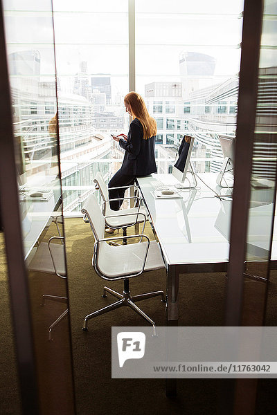 Geschäftsfrau benutzt Mobiltelefon am Bürofenster  London  UK
