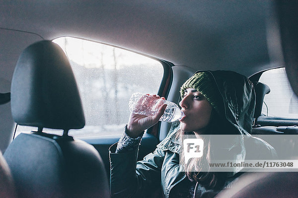 Frau trinkt Wasser auf dem Rücksitz eines Autos