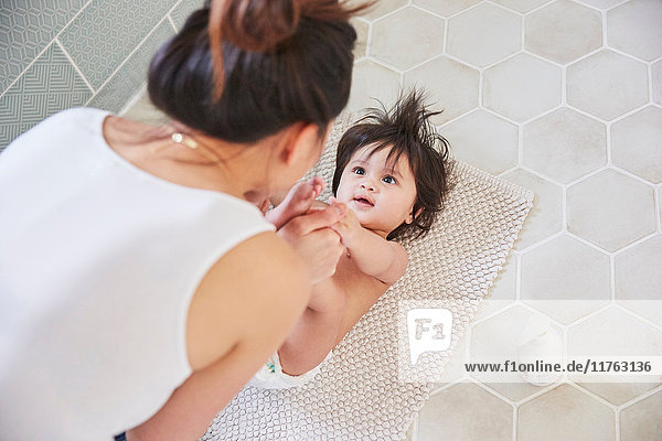 Über-Schulter-Ansicht einer Frau  die mit den Füßen ihrer kleinen Tochter auf dem Badezimmerboden spielt