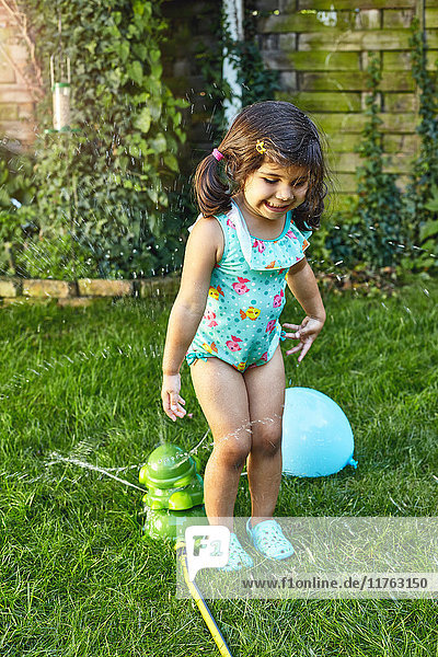 Junges Mädchen spielt im Garten  neben Wassersprinklern