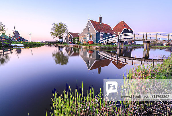 Holzhäuser und Windmühle spiegeln sich im blauen Fluss Zaan bei Sonnenuntergang  Zaanse Schans  Nordholland  Niederlande  Europa