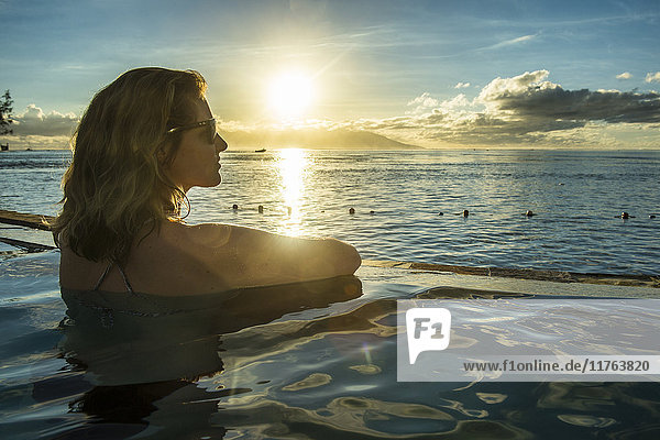 Frau genießt den Sonnenuntergang in einem Schwimmbad mit Moorea im Hintergrund  Papeete  Tahiti  Gesellschaftsinseln  Französisch-Polynesien  Pazifik