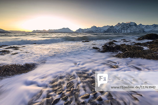 Das Licht des Sonnenuntergangs spiegelt sich auf den Wellen des kalten Meeres  die an die Felsen schlagen  Djupvik  Lyngen Alps  Troms  Norwegen  Skandinavien  Europa