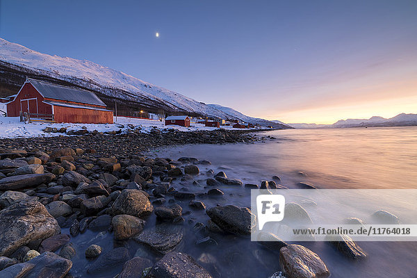 Feuriger Himmel bei Sonnenuntergang und typisches Rorbu  schneebedeckte Gipfel und gefrorenes Meer  Djupvik  Lyngen Alps  Troms  Norwegen  Skandinavien  Europa