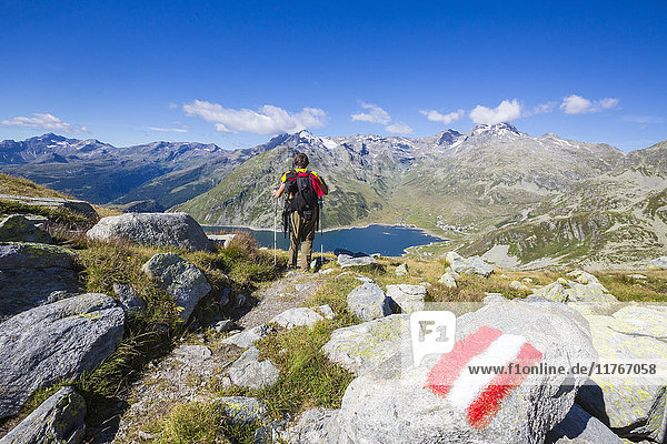 Hiker admires the blue Lake Montespluga and the rocky peaks in summer  Chiavenna Valley  Valtellina  Lombardy  Italy  Europe