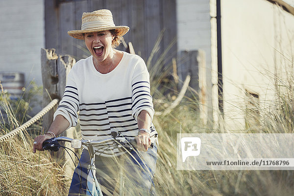 Playful mature woman riding bicycle on beach grass path