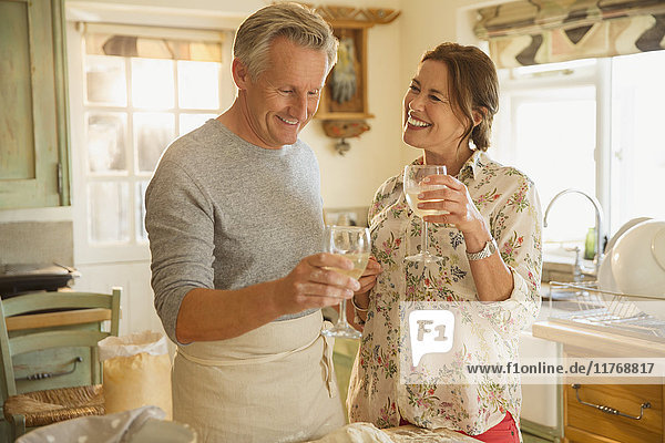 Lächelndes reifes Paar beim Weintrinken und Kochen in der Küche