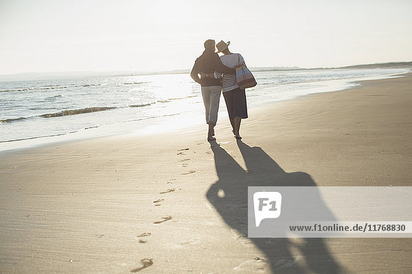 Affectionate mature couple hugging and walking on sunny beach