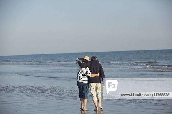 Zärtliches  reifes Paar  das sich umarmt und in der sonnigen Meeresbrandung spazieren geht.